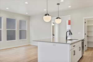 Kitchen featuring sink, white cabinetry, light hardwood / wood-style flooring, pendant lighting, and a kitchen island with sink