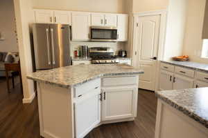 Kitchen with white cabinets, dark hardwood / wood-style floors, a kitchen island, light stone counters, and stainless steel appliances