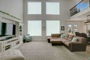 Carpeted living room with built in shelves, a high ceiling, plenty of natural light, and a notable chandelier