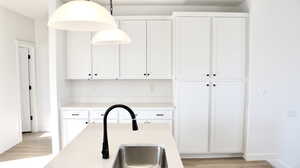 Kitchen featuring white cabinets, decorative light fixtures, light wood-style floors, and sink