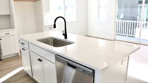 Kitchen featuring white cabinetry, dishwasher, a kitchen island with sink, and sink