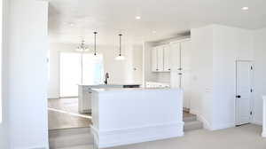 Kitchen featuring a kitchen island, sink, white cabinetry, and hanging light fixtures