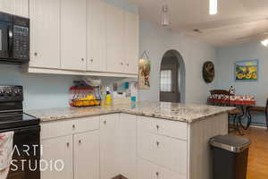 Kitchen featuring kitchen peninsula, light stone counters, ceiling fan, black appliances, and light hardwood / wood-style flooring