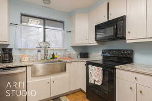 Kitchen with light stone counters, sink, and black appliances