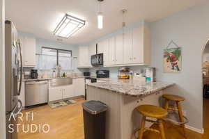 Kitchen with sink, hanging light fixtures, kitchen peninsula, white cabinets, and black appliances