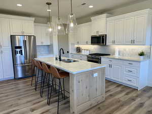 Kitchen with light stone counters, a kitchen island with sink, sink, high quality appliances, and white cabinets