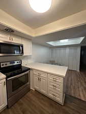 Kitchen with white cabinets, a raised ceiling, appliances with stainless steel finishes, dark hardwood / wood-style flooring, and kitchen peninsula