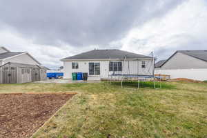 Back of property with a patio area, a yard, a trampoline, and a storage shed