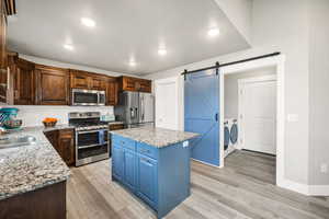 Kitchen with appliances with stainless steel finishes, sink, a barn door, separate washer and dryer, and a center island