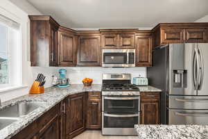 Kitchen with sink, decorative backsplash, light stone countertops, dark brown cabinets, and stainless steel appliances