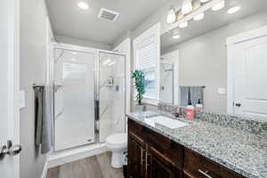 Bathroom with vanity, toilet, wood-type flooring, and a shower with door