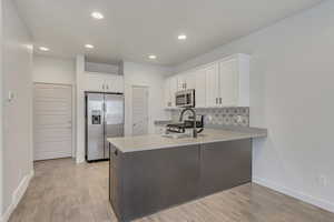 Kitchen featuring white cabinets, kitchen peninsula, backsplash, and appliances with stainless steel finishes