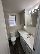 Bathroom featuring shower/tub combo, vanity, a textured ceiling, hardwood / wood-style floors, and toilet