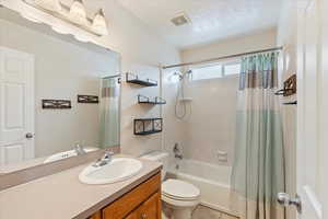 Full bathroom with shower / bath combo, tile patterned floors, a textured ceiling, toilet, and vanity