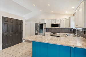 Kitchen with lofted ceiling, sink, tasteful backsplash, white cabinetry, and stainless steel appliances