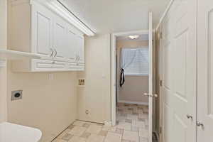 Clothes washing area with cabinets, a textured ceiling, and hookup for an electric dryer