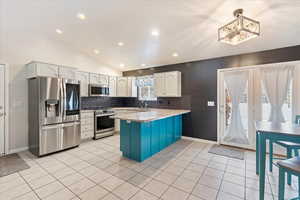 Kitchen featuring hanging light fixtures, white cabinets, stainless steel appliances, and vaulted ceiling