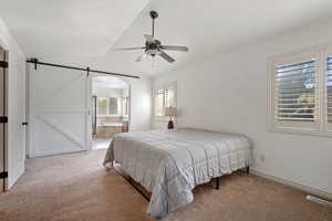 Carpeted bedroom with ceiling fan, a barn door, ensuite bathroom, and vaulted ceiling