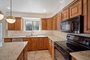 Kitchen featuring black appliances, sink, hanging light fixtures, tasteful backsplash, and light stone counters