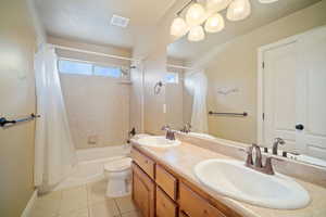 Full bathroom with toilet, shower / tub combo with curtain, vanity, and tile patterned flooring