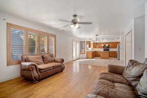 Living room with ceiling fan with notable chandelier, light wood-type flooring, and sink