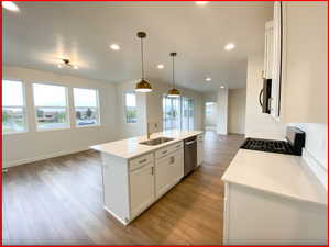 Kitchen featuring sink, decorative light fixtures, white cabinets, light hardwood / wood-style floors, and an island with sink