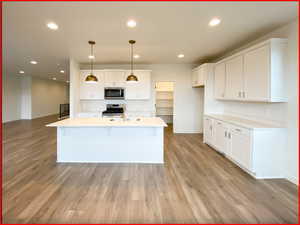 Kitchen featuring decorative light fixtures, light wood-type flooring, white cabinetry, and stainless steel appliances