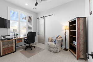 Office space featuring ceiling fan, a barn door, and light colored carpet, plantation shutters, could be 4th bedroom.