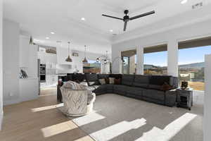 Living room featuring a tray ceiling, red rock views, and ceiling fan with notable chandelier