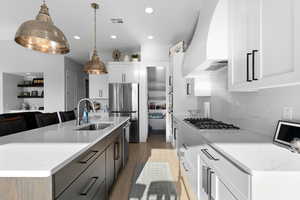 Kitchen featuring white cabinetry, light stone countertops, stainless steel appliances, pendant lighting, and a kitchen island with sink