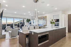 Kitchen with built in microwave, sink, decorative light fixtures, a kitchen island with sink, and hardwood / wood-style flooring