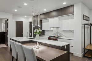 Kitchen featuring tasteful backsplash, a kitchen island with sink, sink, and decorative light fixtures