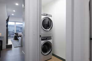 Washroom with stacked washer and clothes dryer and hardwood / wood-style flooring