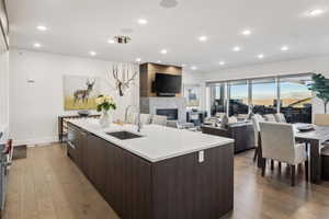 Kitchen with dark brown cabinetry, sink, hanging light fixtures, an island with sink, and a tiled fireplace