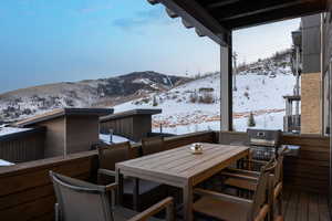 Snow covered deck with a mountain view and area for grilling