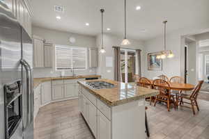 Kitchen featuring decorative backsplash, appliances with stainless steel finishes, decorative light fixtures, white cabinets, and a center island