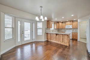 Kitchen featuring light stone countertops, backsplash, kitchen peninsula, a chandelier, and white appliances