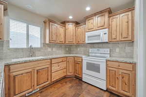 Kitchen featuring white appliances, dark wood-type flooring, sink, decorative backsplash, and light stone counters