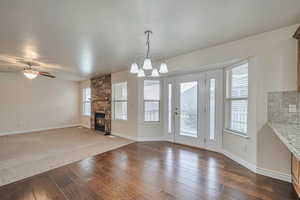 Unfurnished dining area with a stone fireplace, dark hardwood / wood-style floors, and ceiling fan with notable chandelier