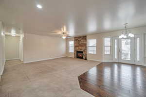 Unfurnished living room with ceiling fan with notable chandelier, a fireplace, and light carpet