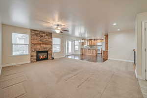 Unfurnished living room with ceiling fan, a stone fireplace, and light carpet