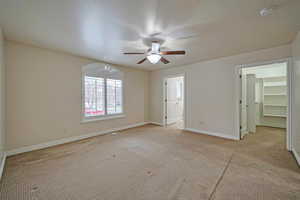 Unfurnished bedroom with ceiling fan, a walk in closet, light carpet, and a closet