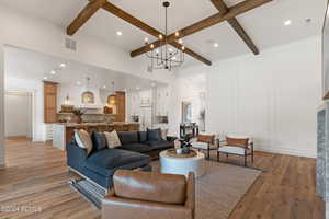 Living room featuring beam ceiling, light wood-type flooring, and an inviting chandelier