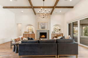 Living room with a large fireplace, coffered ceiling, beamed ceiling, a chandelier, and light hardwood / wood-style floors