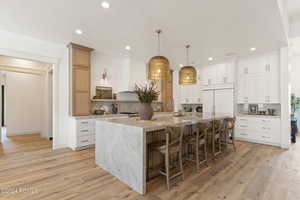 Kitchen featuring paneled refrigerator, backsplash, a spacious island, white cabinets, and light hardwood / wood-style floors