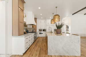 Kitchen featuring pendant lighting, range with two ovens, a spacious island, light hardwood / wood-style flooring, and white cabinetry