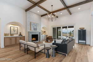 Living room with light wood-type flooring, beam ceiling, a towering ceiling, a notable chandelier, and a large fireplace