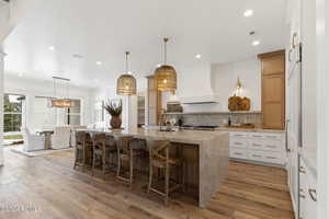 Kitchen with custom exhaust hood, sink, decorative light fixtures, white cabinetry, and a large island