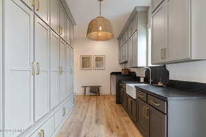 Kitchen with sink, hanging light fixtures, gray cabinets, tasteful backsplash, and light hardwood / wood-style floors