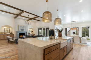 Kitchen featuring a large fireplace, a center island with sink, pendant lighting, and beam ceiling